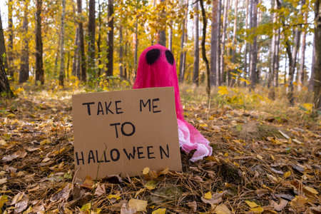 Cardboard TAKE ME TO HALLOWEEN text Creative handmade Halloween holiday decoration. pink ghost in autumn leaves forest. Zero waste homemade decor. Mystic placeの写真素材