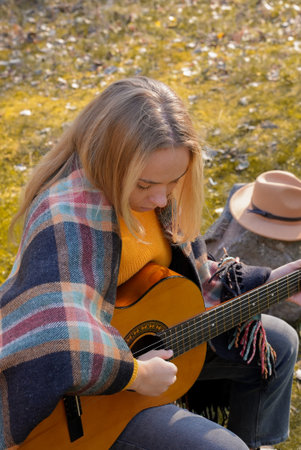 Blonde woman playing string guitar outdoors in autumn forest. Concept of sound therapy, mental...