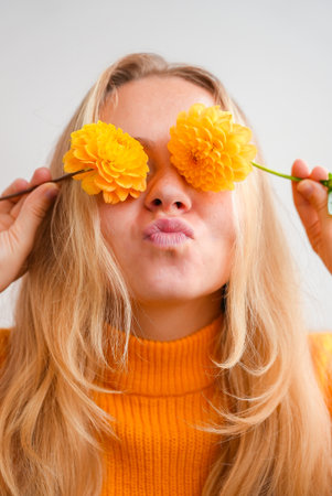 Woman in yellow sweater close her eyes with yellow dahlia Selective focus Bush of autumnal orange...