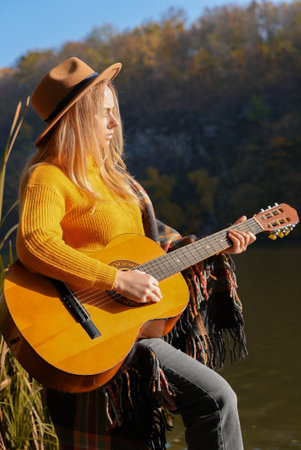 Blonde woman playing string guitar outdoors in autumn forest. Concept of sound therapy, mental...