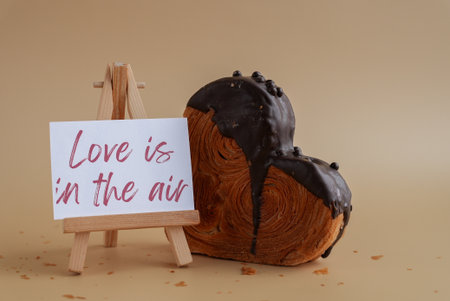 LOVE IS IN THE AIR message on greeting card Delicious fresh croissant topped with Dark chocolate flavor Ganache. Creation unique heart shape bakery. Puff pastry holiday love gift present idea Valentines dayの写真素材