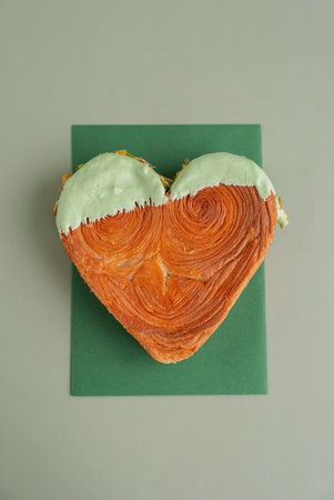 Delightful and vibrant heartshaped pastry croissant treat, beautifully topped with colorful frosting nut galore. Mock up template copy space. Food experimentation viral dessert creativeの写真素材