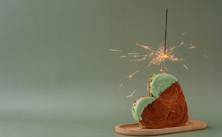 Shiny festive candle sparkler birthday celebration holiday Delightful and vibrant heartshaped pastry croissant treat, beautifully topped with colorful frosting nut galore. Mock up template copy space. Food experimentation viral dessert creativeの写真素材