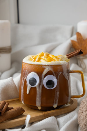Halloween funny faces eyes on cup of beverage Autumn hygge Orange Cup of warm coffee autumn leaves on table. Cozy fall still life footage burning candles. Thanksgiving holidayの写真素材