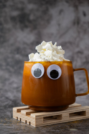 Halloween funny faces eyes on cup of beverage Autumn hygge Orange Cup of warm coffee. Cozy fall still life dark background. Thanksgiving holidayの写真素材