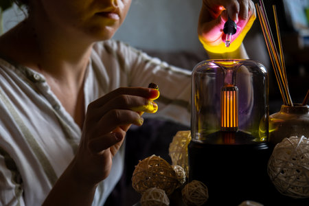 Female hands adding essential oil to Home fragrance aromatic diffuser with essential oil. Modern air humidifier at home. Improving the comfort of wellbeing living in house. Ultrasonic aroma perfume steamの写真素材