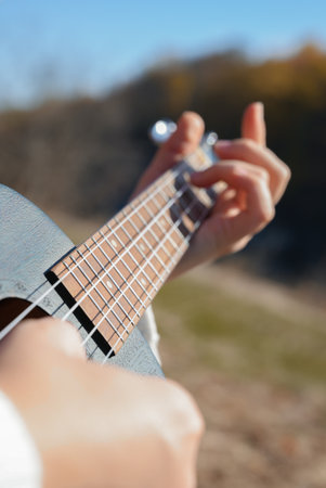 Close up of female hands play ukulele in autumnal park. Young woman plays guitar musical instrument outside in nature fall time.の写真素材