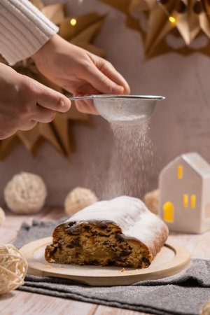 Homemade Christmas traditional cake pie with falling sugar powder with marzipan nuts and dried fruits pastry dessert stollen. Winter holidays season atmosphere. Delicious tasty composition home table settingの写真素材