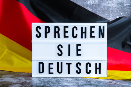 Lightbox with text SPRECHEN SIE DEUTSCH DO YOU SPEAK GERMAN National symbol of Germany. German wave silky flag background. education and learning languagesの写真素材