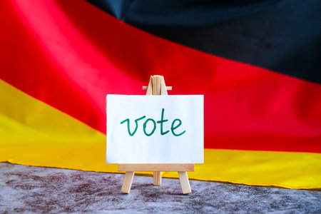 Paper note with words VOTE on National symbol of Germany. German wave silky flag background....