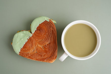 Nutrient-rich matcha drink with Green latte Matcha tea coffee with Delightful and vibrant heartshaped pastry croissant treat, beautifully topped with colorful frosting nut galore. Mock up template copy space. Food experimentation viral dessert creativeの写真素材