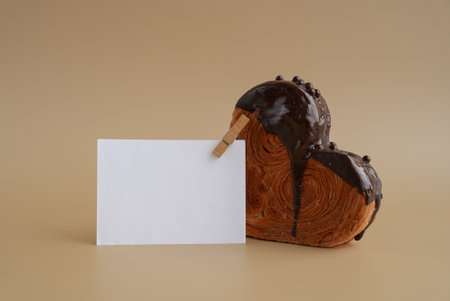 Mock up template paper note card Heart shaped dark chocolate croissant on beige background with copy space. Puff pastry new trendy sweet dessert bakery.の写真素材