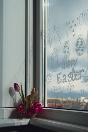 HAPPY EASTER text on creative painted window with white marker. Easter bunny rabbit decoration on...