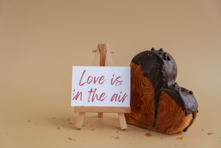 LOVE IS IN THE AIR saying caption on greeting card Delightful heartshaped pastry croissant treat, beautifully topped with colorful frosting galore. Copy space. Food experimentation viral dessert creative baking trendの写真素材