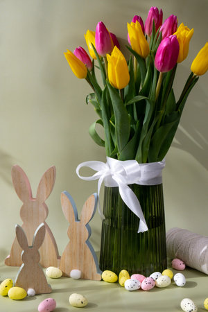 Happy EASTER composition wooden bunny eggs Multicolored fresh tulips in vase in green background...