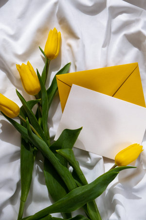 Empty white envelope mock up template for greeting card. Fresh bouquet of yellow tulip flowers on...