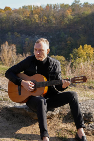 Portrait of smiling caucasian artist plays wooden acoustic guitar in autumnal park. Young songwriter...