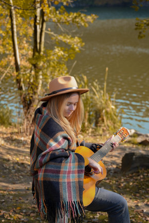Portrait of smiling caucasian artist plays wooden acoustic guitar in autumnal park. Young songwriter plays string musical instrument hobby outside in nature fall time.の写真素材