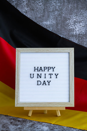 Letter board with message HAPPY UNITY DAY National symbol of Germany. German wave silky flag background. Historical remembrance and public holiday