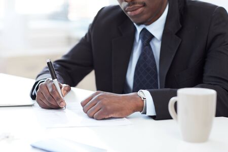 Close-up of African businessman sitting at office desk holding pen and signing a business contract