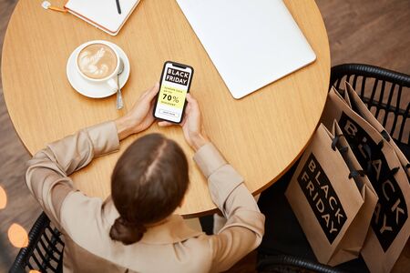 High angle view of young woman sitting at the table with shopping bags and using her mobile phone in...