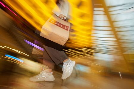 Blurred motion of young woman with paper shopping bags doing shopping during sale in the store