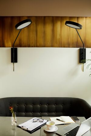 Image of workplace with laptop computer and documents with modern lamps above the table at office