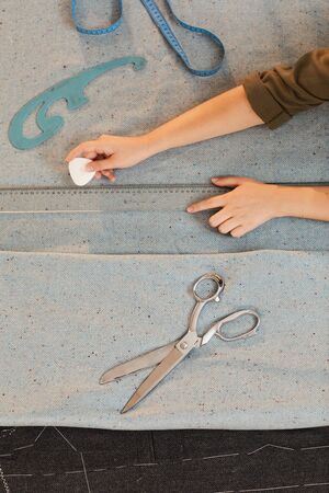 Close-up of hands of tailor using chalk and ruler and drawing pattern on fabric at the table