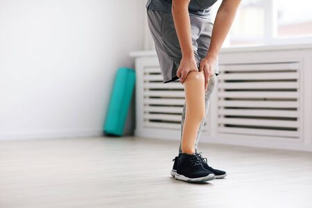 Close-up of young disabled man standing and wearing prosthesis on his leg in the room