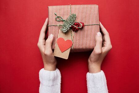 Close-up of woman holding gift box with greeting card for Valentine's Day isolated on red backgroundの写真素材