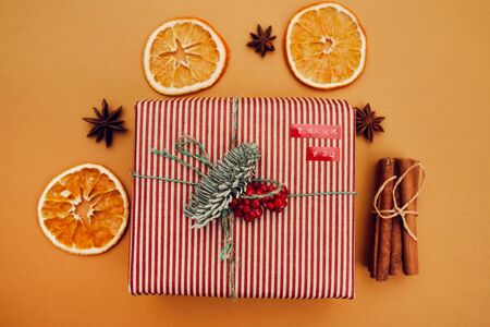 Close-up of Christmas present decorated with fir branch and red berries with dried orange and cinnamon around isolated on orange backgroundの写真素材