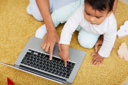 Close-up of child typing on computer keyboard on laptop with mother sitting near by him and teaching himの写真素材