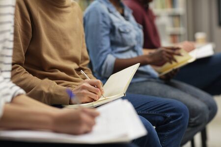 Close-up of group of people sitting on chairs and making notes in notebooks during seminarの写真素材