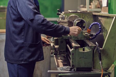 Close-up of man in workwear standing near the machine and working on it in the plant