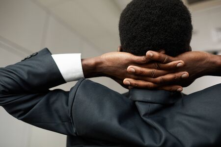 Rear view of young African businessman in suit holding his hands behind his head and relaxing after workの写真素材