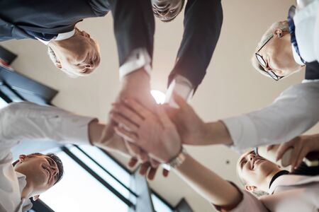 Low angle view of business team holding hands and cooperating with each other during team work at officeの写真素材
