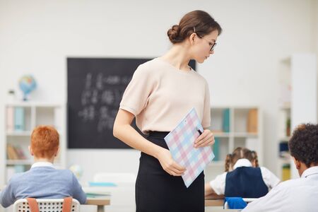 Young teacher watching for the work of school children while teaching them at schoolの写真素材