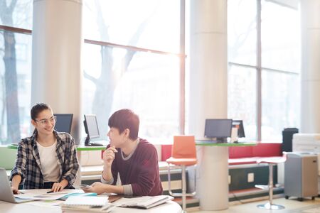 Young woman and young man sitting at the table in front of laptop and discussing their homework together in computer classの写真素材