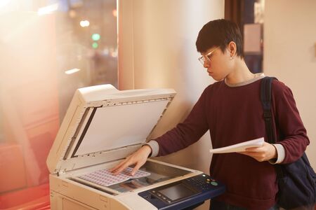 Asian college student making copy of new material using printer at universityの写真素材