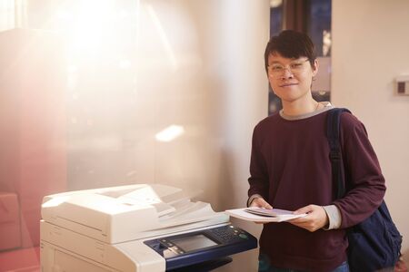 Portrait of Asian young man in eyeglasses holding documents and smiling at camera he is going to...