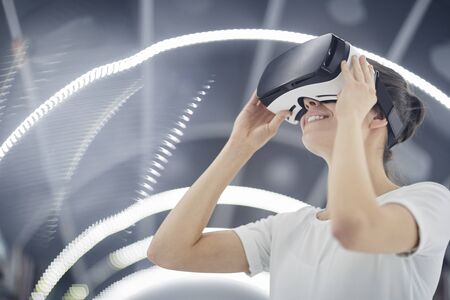 Young woman wearing virtual glasses smiling while playing in virtual video game