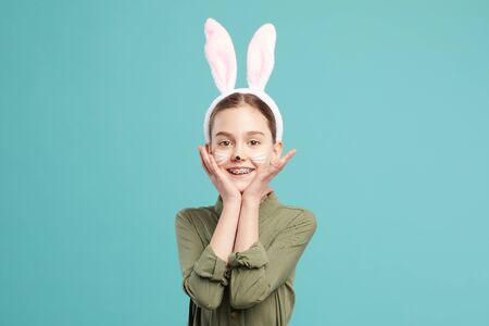 Portrait of little girl in rabbit ears posing at camera against the blue backgroundの写真素材