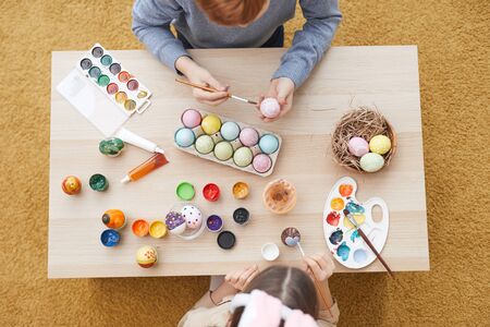High angle view of two children sitting at the table and painting eggs for Easter holiday togetherの写真素材