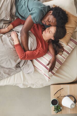 Affectionate young couple lying on bed embracing each other and sleeping at homeの写真素材