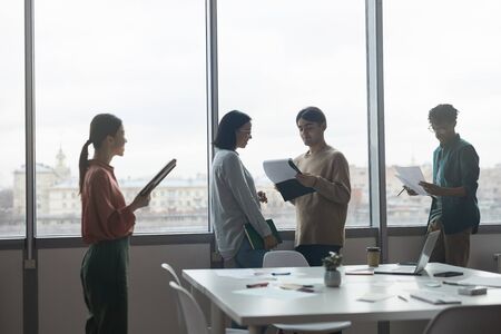 Business team standing in front of big windows and doing their work during work day at office