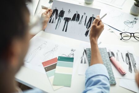 Close-up of man sitting at the table and looking at sketches of clothes in his hands during his work at officeの写真素材