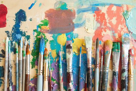 Close-up of different paintbrushes in paints lying on the paintingの写真素材