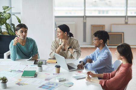 Multiethnic group of business team sitting at the table wtih laptop and business graphics and...