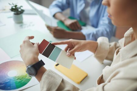 Close-up of businesswoman holding colored palette and choosing a color while sitting at the table...