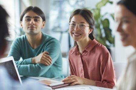 Young businesswoman in eyeglasses smiling and talking to her colleagues during business meeting at officeの写真素材